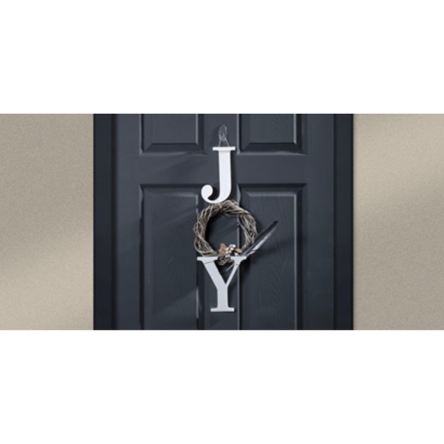 Eine schwarze Tür zeigt große weiße Buchstaben "J" und "Y" mit einem kleinen braunen Kranz - aufgehängt von einem 3M Deutschland GmbH Command™ transparenter, mittelgroßer, ovaler Haken (Außenbereich, 17091AW) - dazwischen, um "JOY" zu schreiben. Der Hintergrund ist eine schlichte hellbraune Wand.