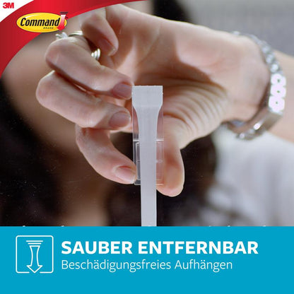 Une personne tire l'onglet d'une bande résistante à l'eau Command™ (Multipack : 8×S, 4×M, 4×L) d'un crochet, montrant ainsi le retrait facile et propre sans perçage. Les logos 3M et Command sont visibles.
