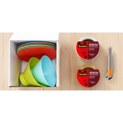 Une boîte avec des assiettes et des bols colorés est placée à côté de deux rouleaux de ruban adhésif d'emballage Scotch® pour une fermeture sécurisée (50 mm x 66 m) de 3M Deutschland GmbH, un transparent et un marron, ainsi qu'un cutter universel sur une surface en bois clair.