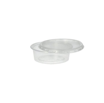 Un gobelet Starpak 50 Dressing, PP rond Ø 7,1 cm transparent avec un couvercle transparent assorti est légèrement incliné sur un fond blanc simple - idéal pour le service traiteur.
