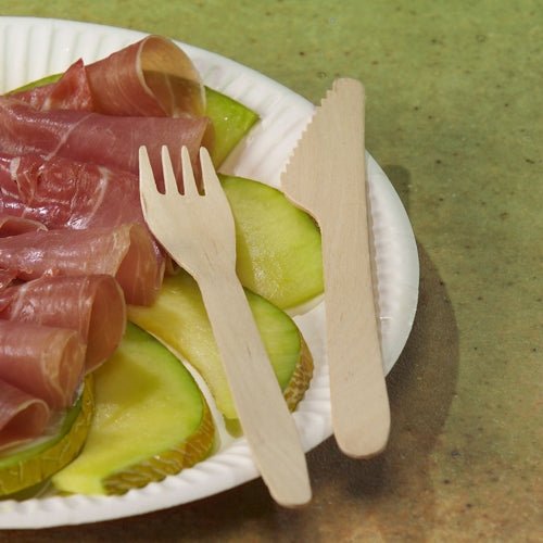 Une assiette en carton de PAPSTAR GmbH avec des tranches de pomme verte et de la viande salée roulée est garnie de fourchettes PAPSTAR en bois FSC® "pure", 16,5 cm, écologiques. L'assiette repose sur un support vert.