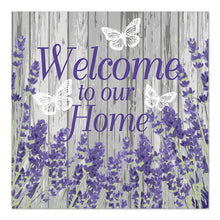 Schild mit violettem Text "Welcome to our Home" auf grauem Holzhintergrund, verziert mit lavendelfarbenen Blumen und drei weißen Schmetterlingen, in Anlehnung an PAPSTAR 20 Servietten, 33x33cm, 3-lagig von PAPSTAR GmbH.