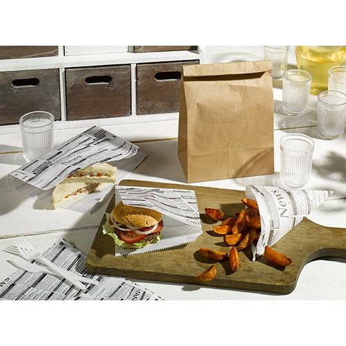 Sur une feuille de papier d'emballage servant de substitut au parchemin, de 35 x 25 cm, résistante à la graisse, la PAPSTAR Sur la table dressée par la GmbH sont disposés un sandwich, un hamburger et des quartiers de pommes de terre ; à côté se trouvent des gobelets transparents, un sac en papier marron, une cruche contenant une boisson jaune et des couverts en plastique blanc.