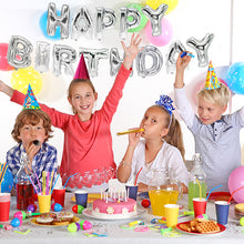 Quatre enfants avec des chapeaux de fête célèbrent un anniversaire à une table décorée avec un gâteau et des articles de fête. Derrière, l'ensemble de ballons métalliques « Joyeux Anniversaire » de la société PAPSTAR en argent et des ballons colorés décorent le mur.