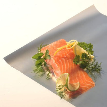 Deux filets de saumon cru reposent sur une feuille de papier d'aluminium Starpak en vrac de Starpak, garnis d'aneth frais, de persil, de zeste de citron et de tranches de citron vert, devant un fond simple et clair.