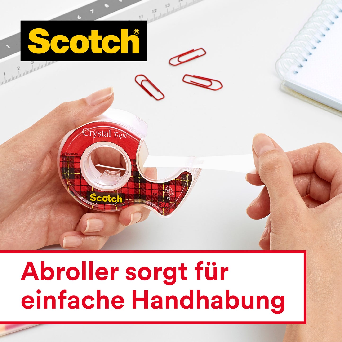 Eine Person benutzt das 3M Deutschland GmbH Scotch® Crystal Klebeband (19 mm x 12 m, 2 Rollen auf Abrollern + 3,2 m GRATIS), um transparentes Klebeband herauszuziehen. Büroklammern, ein Lineal und ein Notizbuch liegen auf einem weißen Schreibtisch mit deutschem Text darunter.