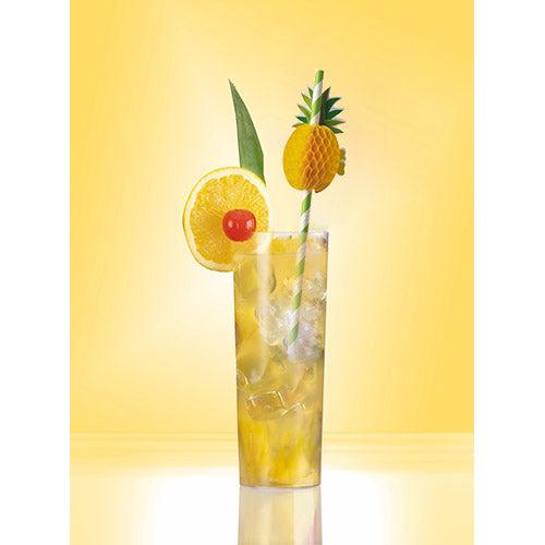 Un grand verre avec une boisson glacée jaune, garni de citron, cerise, feuille verte et un petit ananas, est décoré d'une paille en papier PAPSTAR 50 de la société PAPSTAR GmbH. Le fond jaune uni renforce l'attrait rafraîchissant.