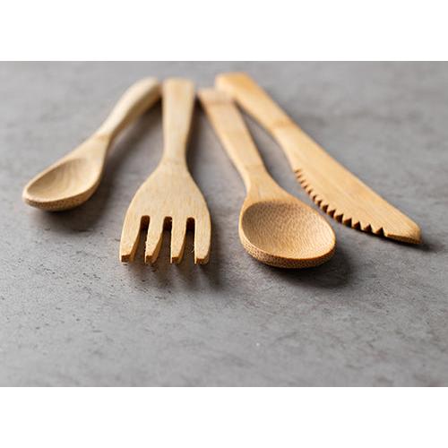 Quatre ustensiles en bois - une cuillère, une fourchette, une autre cuillère et un PAPSTAR couteau en bambou "pure" 16 cm - sont disposés sur une surface en pierre grise. Les couteaux jetables écologiques de PAPSTAR GmbH sont de couleur brun clair et ont une surface lisse et polie.