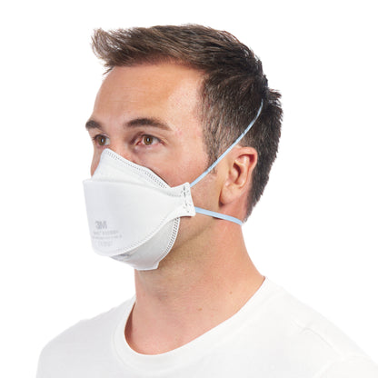 Un homme aux cheveux bruns courts, vu de profil, porte une chemise blanche et un masque de confort à particules 3M™ Aura™ 9320+ FFP2 de 3M Deutschland GmbH, fixé avec des bandes élastiques et sans fente.