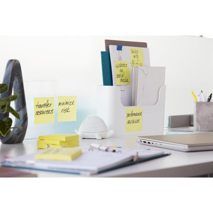 Un bureau moderne avec un ordinateur portable, des fournitures de bureau, un bac à documents blanc, une petite figurine de tortue blanche et des Post-it® Super Sticky Notes Cube (Jaune, 76x76 mm) de 3M Deutschland GmbH avec les inscriptions "Transférer les ressources", "Minimiser le risque" et "Évaluation des performances".
