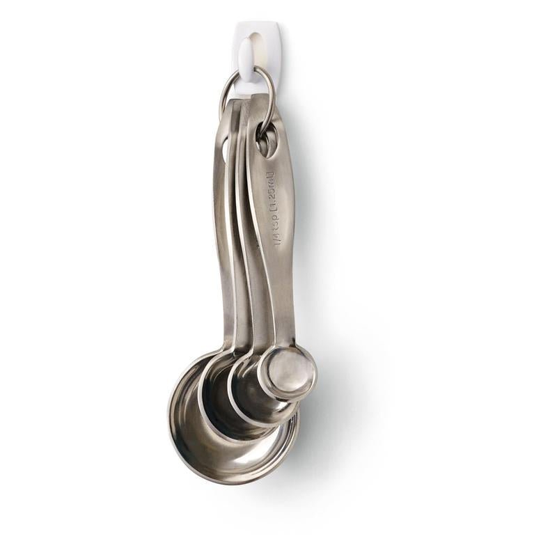 Quatre cuillères doseuses en acier inoxydable accrochées à un anneau métallique pendent à un crochet mini Command™ 17006 de 3M Deutschland GmbH - solidement fixées sans perçage et faciles à enlever de la paroi blanche sans laisser de résidus.