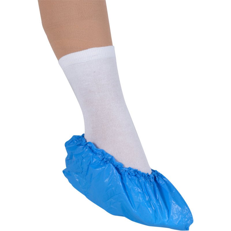 Un pied dans une chaussette blanche est protégé par des surchaussures Abena Re-Seller GmbH, 15 cm 35 my CPE, bleu, qui offrent une protection hygiénique pratique à usage unique.