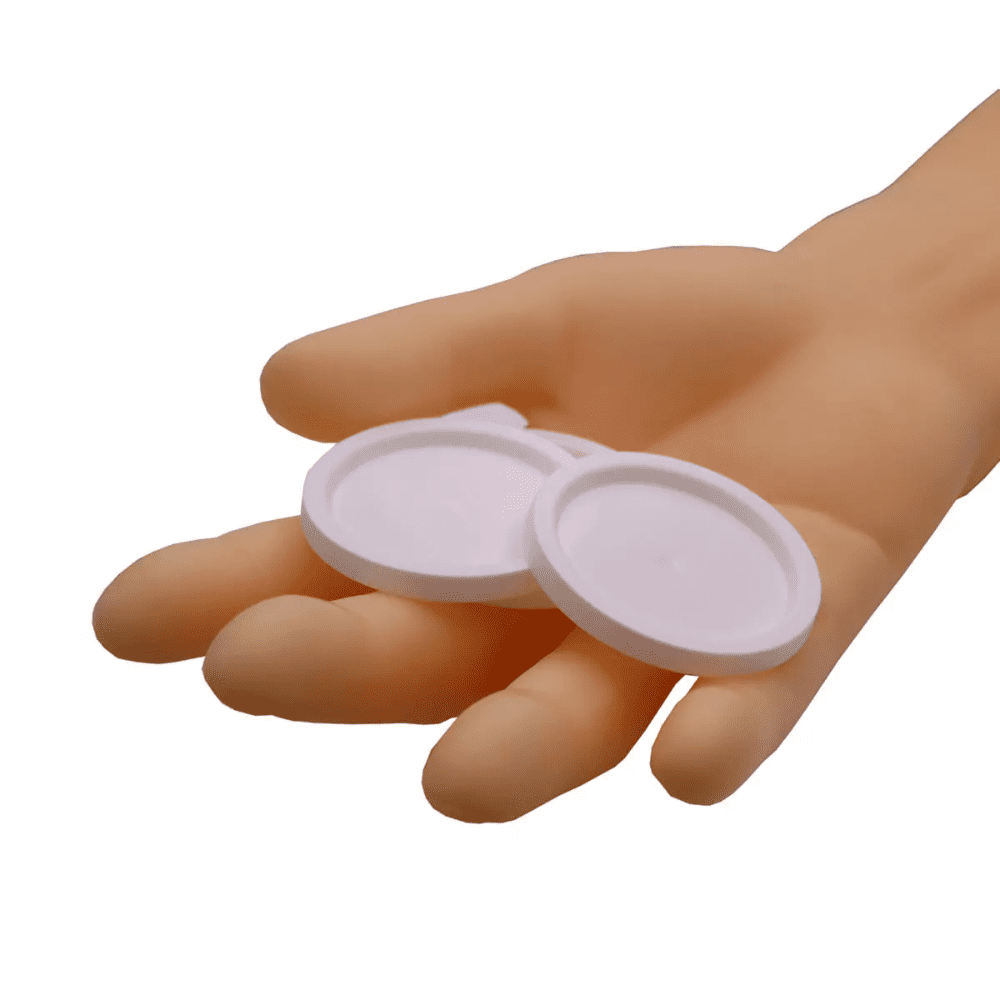 Une main tient deux couvercles ronds AMPri pour gobelets médicaux, objets blancs sur un fond blanc simple.