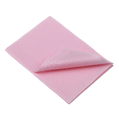 Une serviette de patient jetable AMPri Dental pliée, de couleur rose clair avec une surface texturée, est visible sur un fond blanc. Ce matériau doux et absorbant ressemble aux serviettes dentaires d'AMPri Handelsgesellschaft mbH et est parfait pour nettoyer ou essuyer pendant le traitement dentaire.