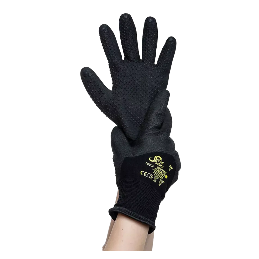 Une paire de gants de protection résistants au froid AMPri SolidSafety Tough Winter Dots noirs avec des paumes texturées est tenue en l'air par une main. Ces gants, conçus pour améliorer la dextérité fine, portent au dos la marque jaune et les signes de certification de sécurité de la société commerciale AMPri mbH.