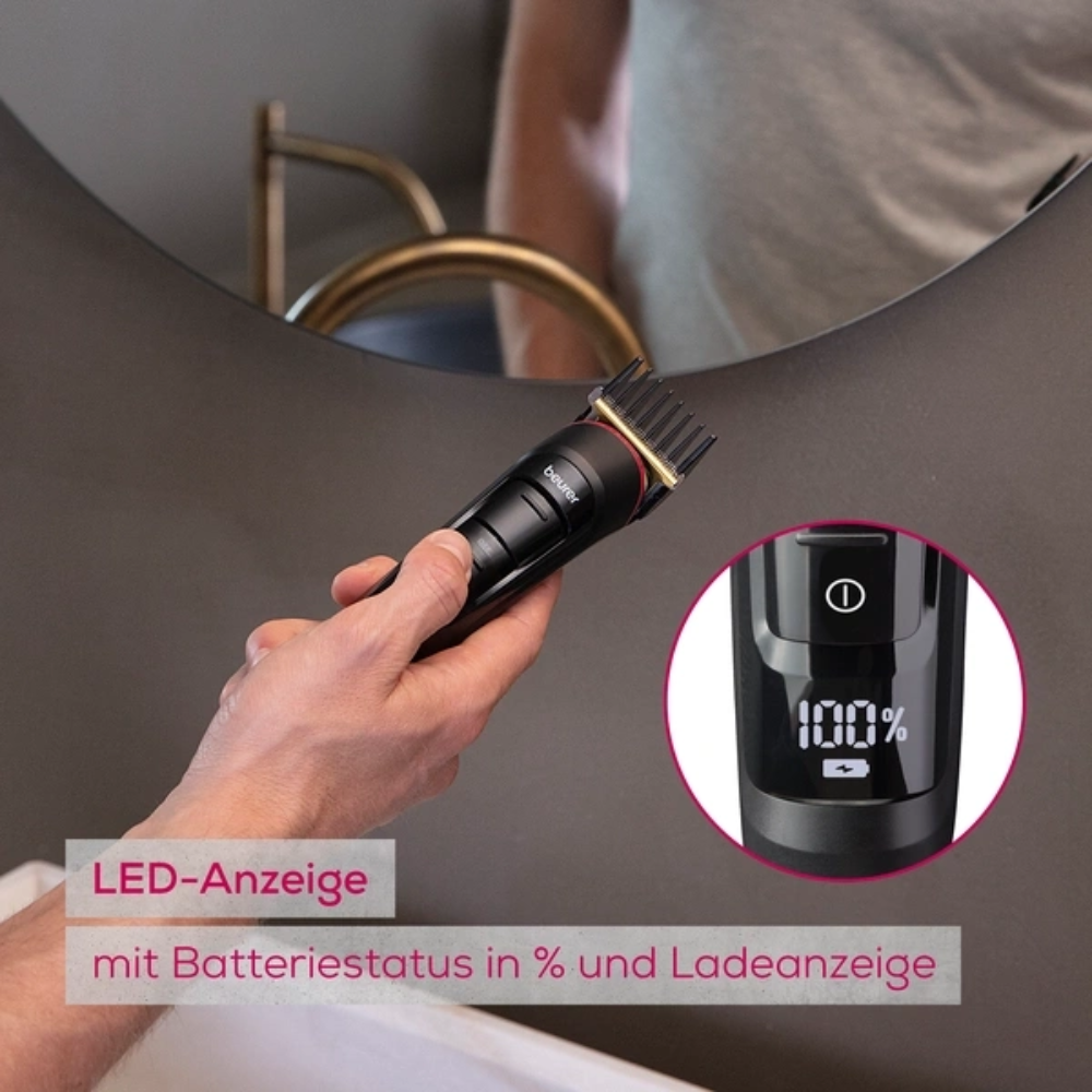 Une main tient l'article discontinué Beurer Multigroomer MN9X de Beurer GmbH avec écran LED, qui affiche le niveau de la batterie, devant le miroir de la salle de bain. L'inscription allemande indique l'appareil étanche et l'état de charge.