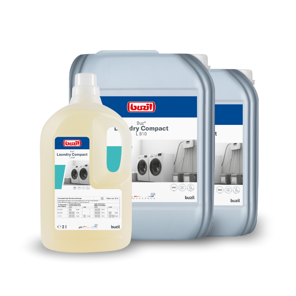 Exposées sont trois contenants avec Buzil Buz® Laundry Compact L 810 Détergent liquide hautement concentré de BUZIL-WERK Wagner GmbH & Co. KG. Devant, une petite bouteille claire, derrière deux plus grands contenants gris. Sur chaque contenant se trouvent des étiquettes avec des textes et des images de machines à laver, indiquant la fonction du détergent dans l'entretien textile professionnel.