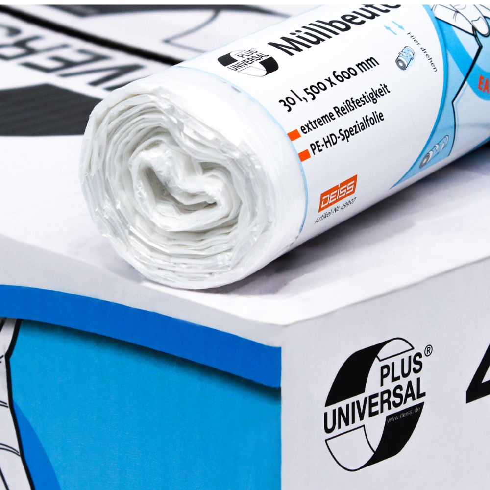 Un rouleau de sacs poubelle DEISS Universal Plus® de 30 litres, d'EMIL DEISS KG (GmbH + Co.) avec des inscriptions bleues et orange repose sur un carton. Le texte contient « sacs poubelle » ainsi que des informations sur le film spécial HDPE, les dimensions et le matériau. En arrière-plan, un autre rouleau est partiellement visible.