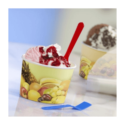 Un pot de glace Starpak décoré de motifs de fruits avec deux boules de crème fouettée et une sauce aux baies, ainsi qu'une cuillère rouge. À côté, une cuillère en plastique bleue repose sur la table.
