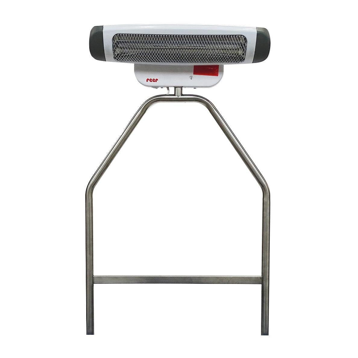 Sur le support en acier inoxydable Novocal pour radiateurs, un radiateur électrique blanc-gris avec une grille métallique et le logo rouge "reer" est monté, ce qui le rend idéal comme accessoire dans la zone de changement pour une fixation sécurisée à une table à langer.