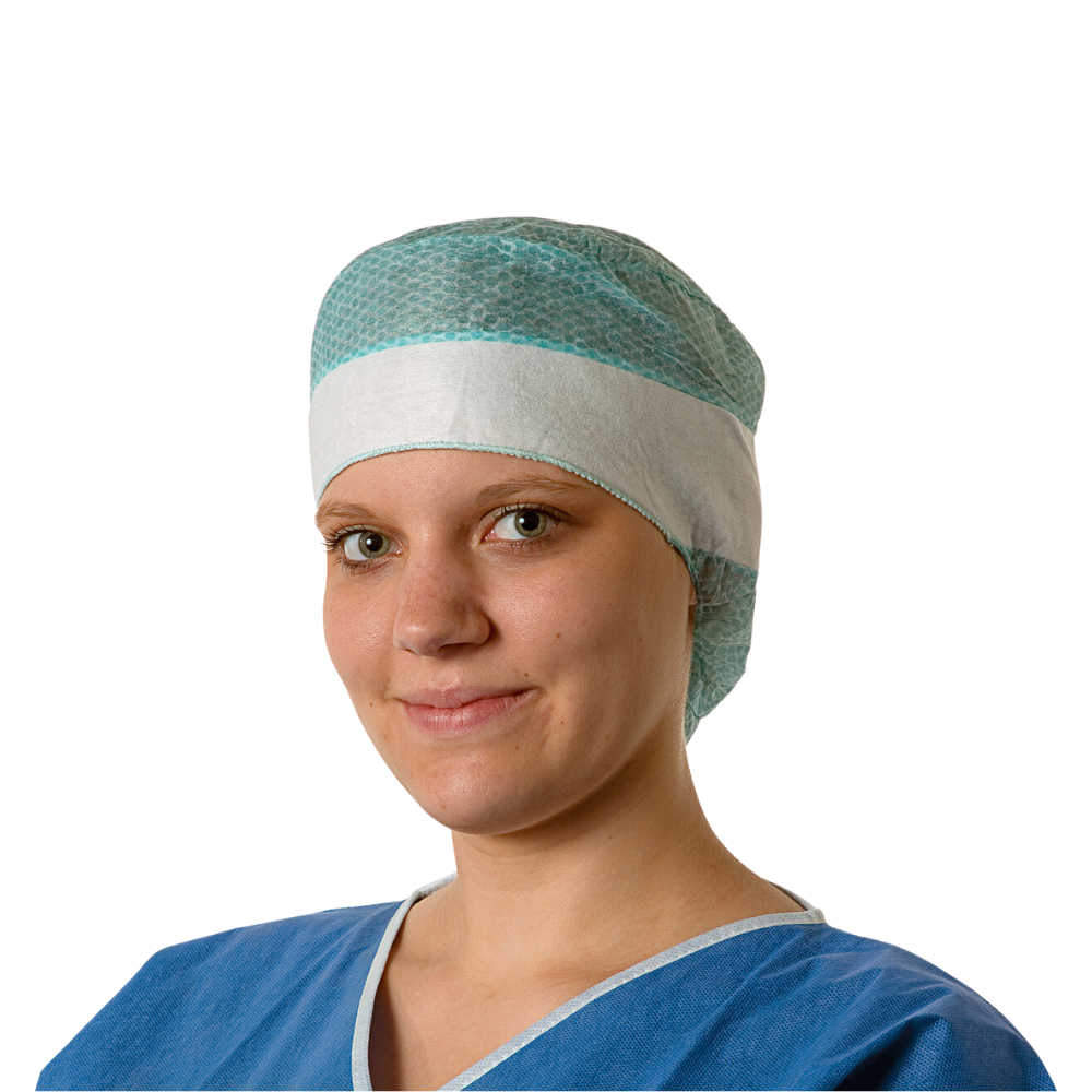Une jeune médecin porte une blouse chirurgicale bleue et une coiffe jetable Hartmann Foliodress® Cap Comfort Form Plus en tissu non tissé en viscose respirant et sourit doucement à la caméra. L'arrière-plan est simplement blanc.