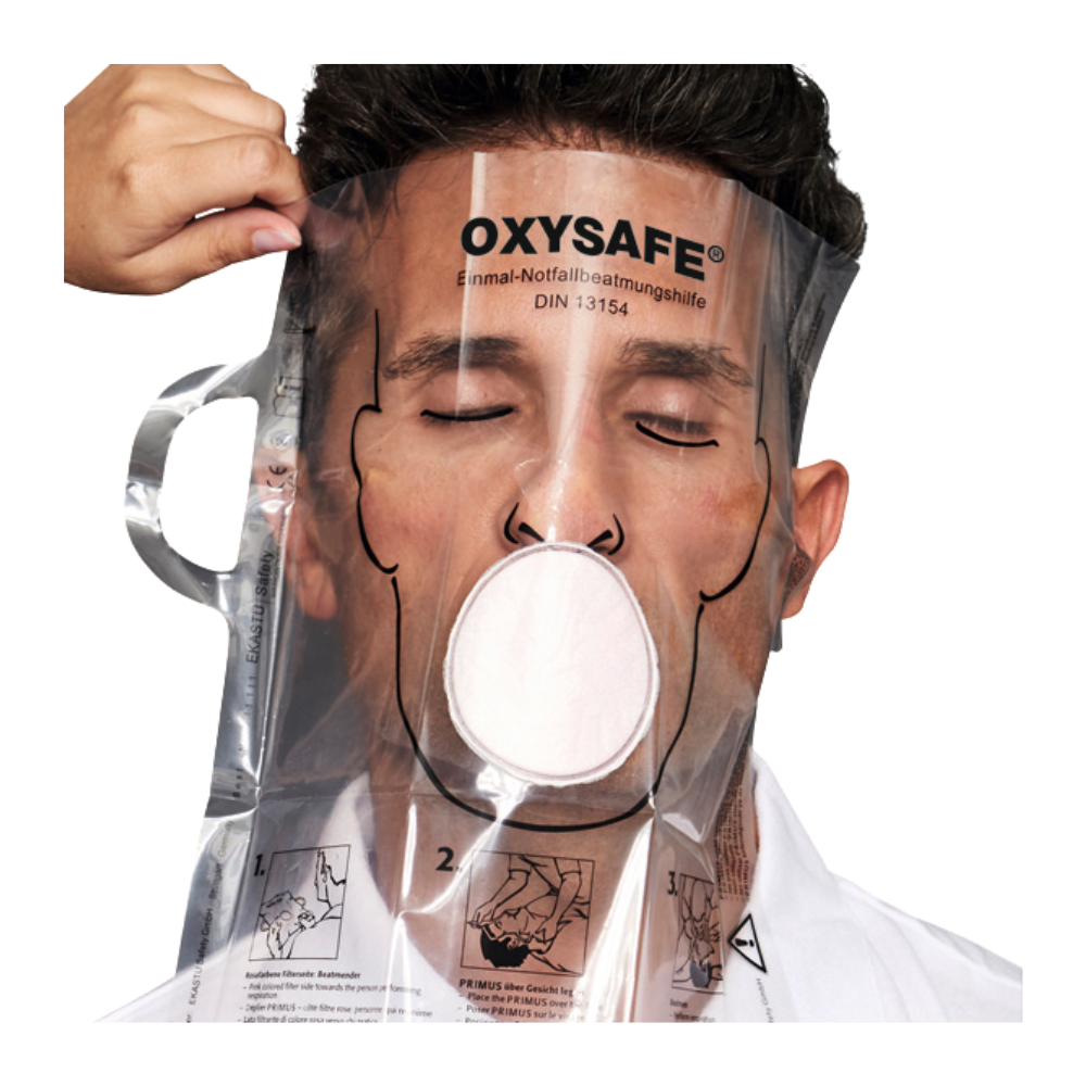 Une personne porte un masque de réanimation d'urgence transparent Holthaus Oxysafe® de Holthaus Medical GmbH & Co. KG et a les yeux fermés, tandis qu'une autre personne ajuste le masque. Le produit est accompagné d'instructions et de diagrammes imprimés sur la surface en plastique.