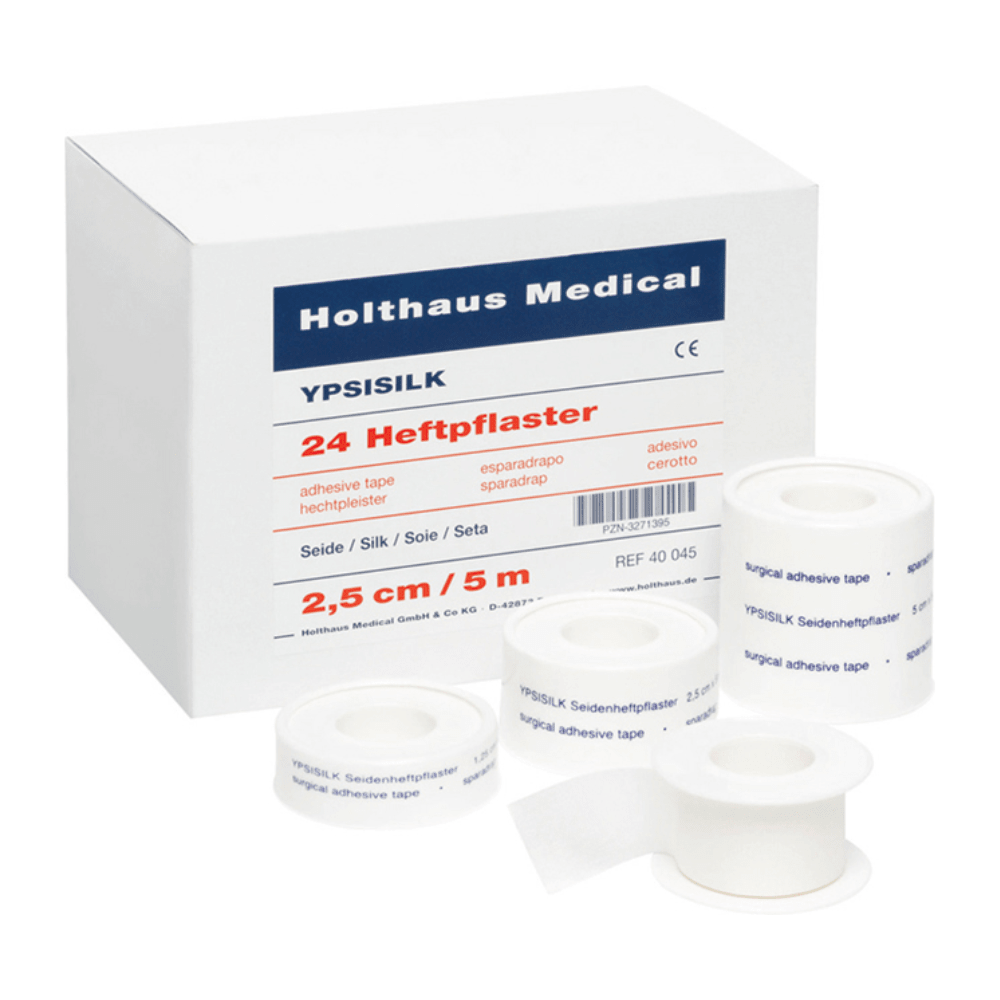 Une boîte portant la mention « Holthaus Medical GmbH & Co. KG » avec la mention « Holthaus YPSISILK Pansements adhésifs – 2,5 cm x 5 m | Paquet (5 m) » et, devant celle-ci, plusieurs rouleaux de ruban adhésif blanc de différentes tailles. Le texte figurant sur la boîte et sur les rubans contient des informations sur le produit en plusieurs langues.