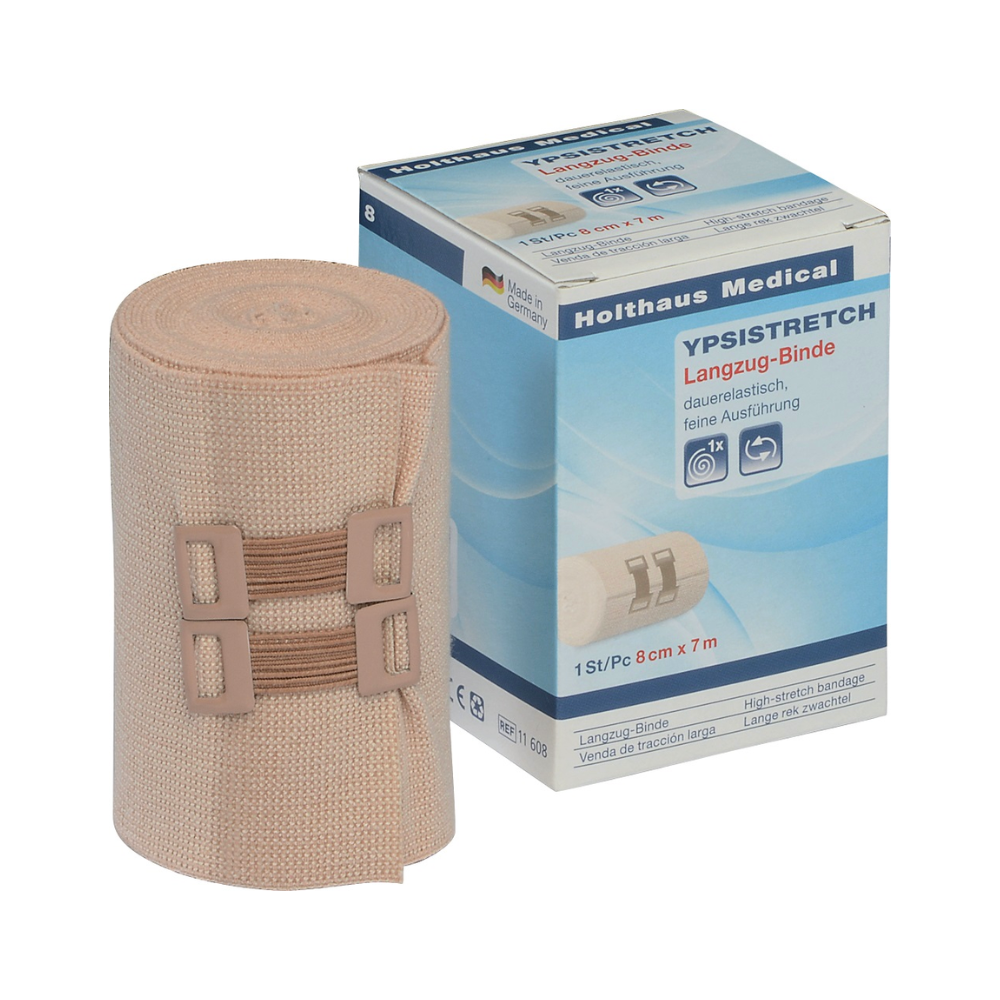 Un bandage Holthaus Ypsistretch Langzug, délicatement à côté de son emballage. Le bandage beige, permanent élastique, est enroulé avec deux fermetures assorties. L'emballage montre des informations sur le produit et une image du bandage, soulignant son utilisation comme outil médical essentiel. Les dimensions sont de 8 cm x 7 m par Holthaus Medical GmbH & Co. KG.
