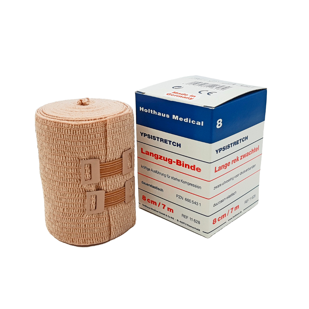 En plus de l'emballage, un bandage élastique médical est illustré. Sur la boîte, il est écrit « Holthaus Ypsistretch Langzug-Binde, kräftig » et les informations sont en allemand. Le bandage couleur chair de Holthaus Medical GmbH & Co. KG offre une compression efficace et est fixé avec deux fermetures en plastique.