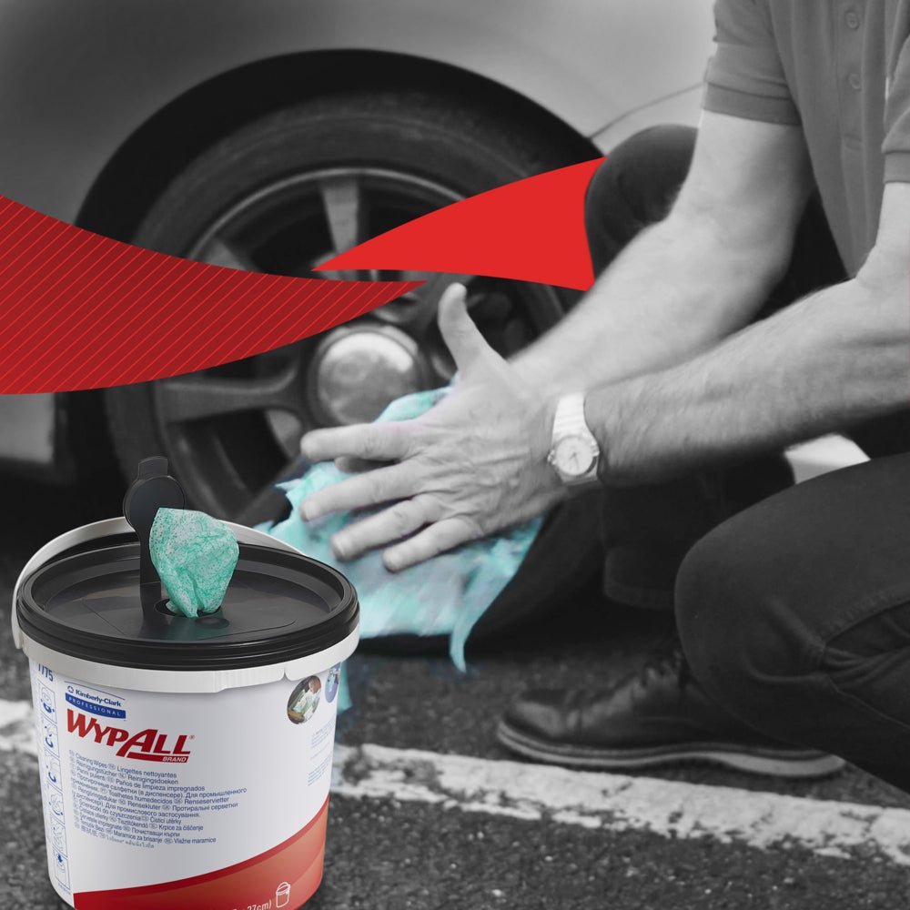Une personne s'agenouille pour nettoyer les roues d'une voiture avec des lingettes vertes WypAll® de Kimberly-Clark GmbH. Au premier plan se trouve un contenant visible avec 6 seaux x 90 feuilles. L'arrière-plan en noir et blanc présente un accent graphique rouge vif.
