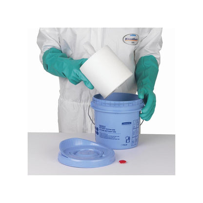 Une personne avec des gants verts et une combinaison blanche place un rouleau de lingettes Kimtech® Wettask™ dans un seau distributeur bleu de Kimberly-Clark GmbH ; le couvercle et le bouchon rouge sont posés sur la table à côté.