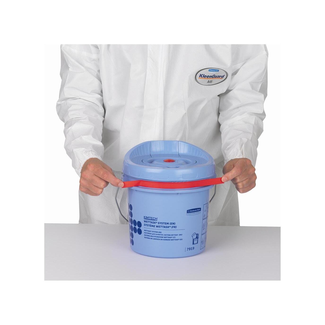 Une personne en combinaison blanche KleenGuard tient un seau distributeur de lingettes en rouleau Kimtech® Wettask™ bleu de Kimberly-Clark GmbH (seau de nettoyage) avec une poignée rouge sur une surface blanche.