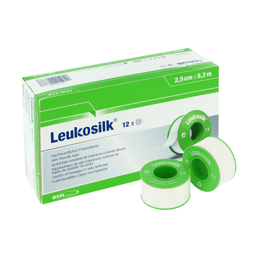 L'image montre une boîte de ruban adhésif Leukosilk de BSN Medical GmbH (9,2 m x 2,5 cm, paquet de 12 rouleaux) avec trois bandes blanches sur des bobines vertes; La boîte multilingue met en avant la fixation facile des bandages et est amovible sans laisser de résidus.