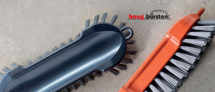 Banner mit zwei Haug Bürsten Scheuerbürsten auf einem Grauen Betonartigen Hintergrund. Inklusive Logo Haug Bürsten