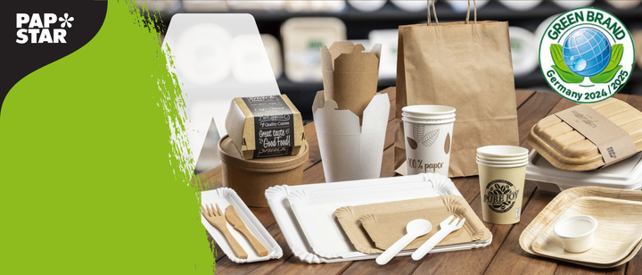 Eine Vielzahl von umweltfreundlichem Einweggeschirr, einschließlich Tellern, Bechern, Tabletts, Schachteln, Besteck und Tüten, aus Papier, Pappe und Holz. Das PAP STAR-Logo und die Plakette Green Brand Germany 2024/2025 sind sichtbar.