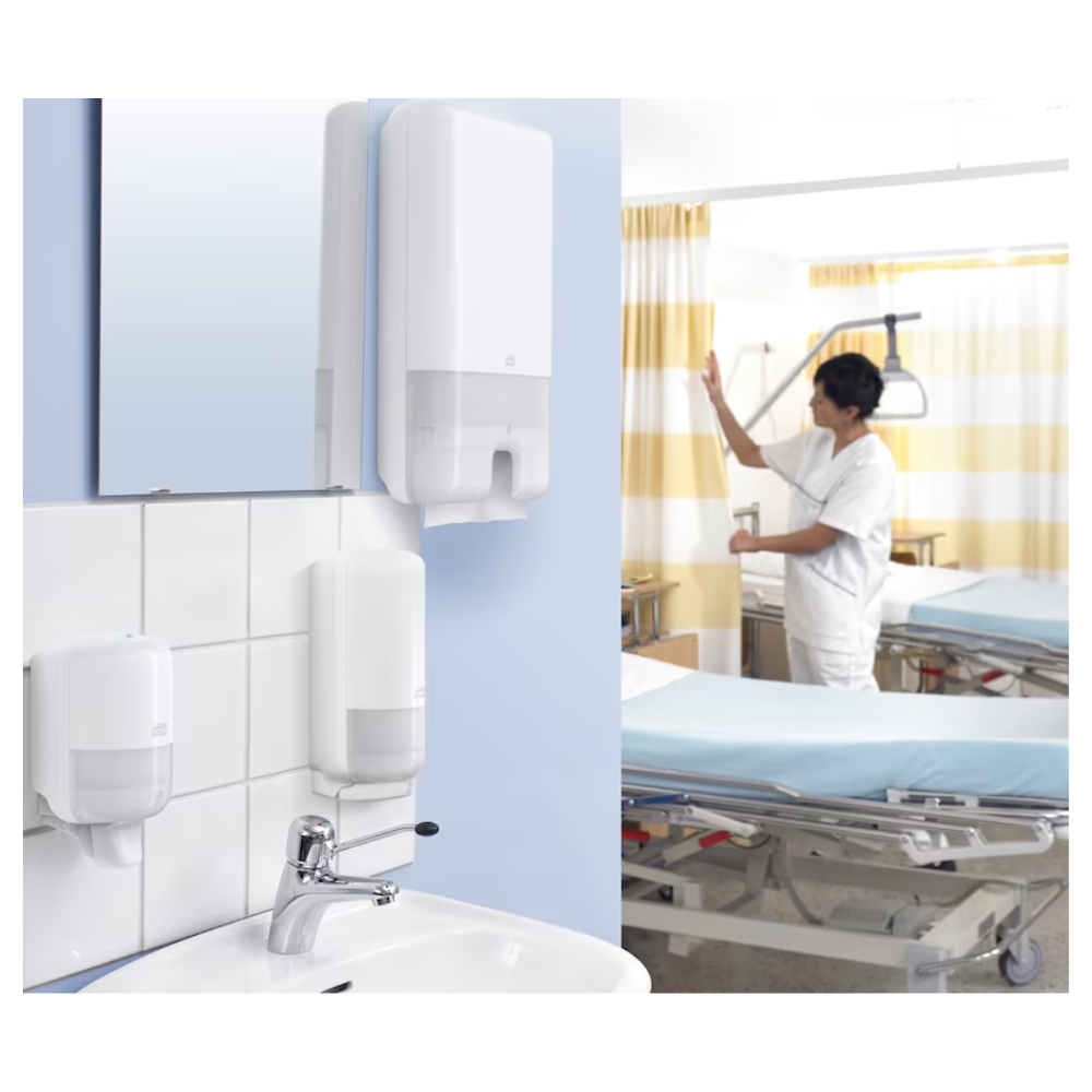 Dans une chambre d'hôpital, un soignant ajuste le rideau à côté du lit d'un patient. Au premier plan se trouvent des serviettes multifold Tork Xpress® 471093 Universal H2 1 pli de TORK – Essity Professional Hygiene Germany GmbH à côté de savon universel. Le lit est recouvert de draps bleus et entouré d'équipements médicaux importants.