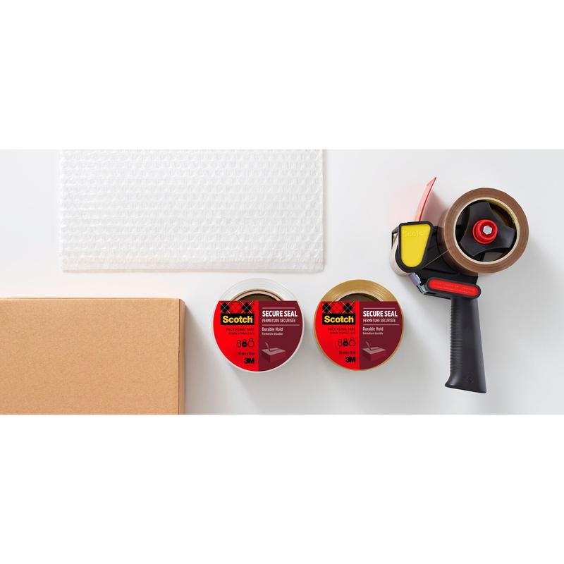 Un carton, du papier bulle, deux rouleaux de ruban adhésif d'emballage Scotch® pour une fermeture sécurisée (50 mm x 66 m) de 3M Deutschland GmbH et un dévidoir à ruban adhésif sont exposés sur une surface blanche.
