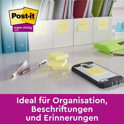 Un bureau avec des stylos, un smartphone, des Post-it® Super Sticky Notes empilés (76 mm x 127 mm, 90 feuilles/bloc, 100% PEFC) de 3M Allemagne GmbH et des dossiers étiquetés avec des notes. Texte allemand : "Idéal pour l'organisation, l'étiquetage et les rappels."