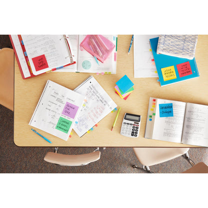 Une table dans une salle de classe, bien ordonnée avec des cahiers ouverts, des manuels, une calculatrice, des stylos colorés, des classeurs et des Notes Post-it® de la Energetic Collection (38mm x 51mm, 100 feuilles/bloc), marque : 3M Deutschland GmbH; trois chaises vides entourent la table.