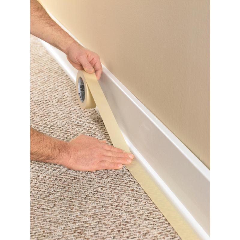 Une personne utilise le ruban de masquage Scotch® Classic, 24 mm x 50 m (70% PEFC) de 3M Deutschland GmbH, pour masquer la plinthe où la moquette rencontre le mur, afin de protéger le revêtement lors des travaux de peinture et de rénovation.