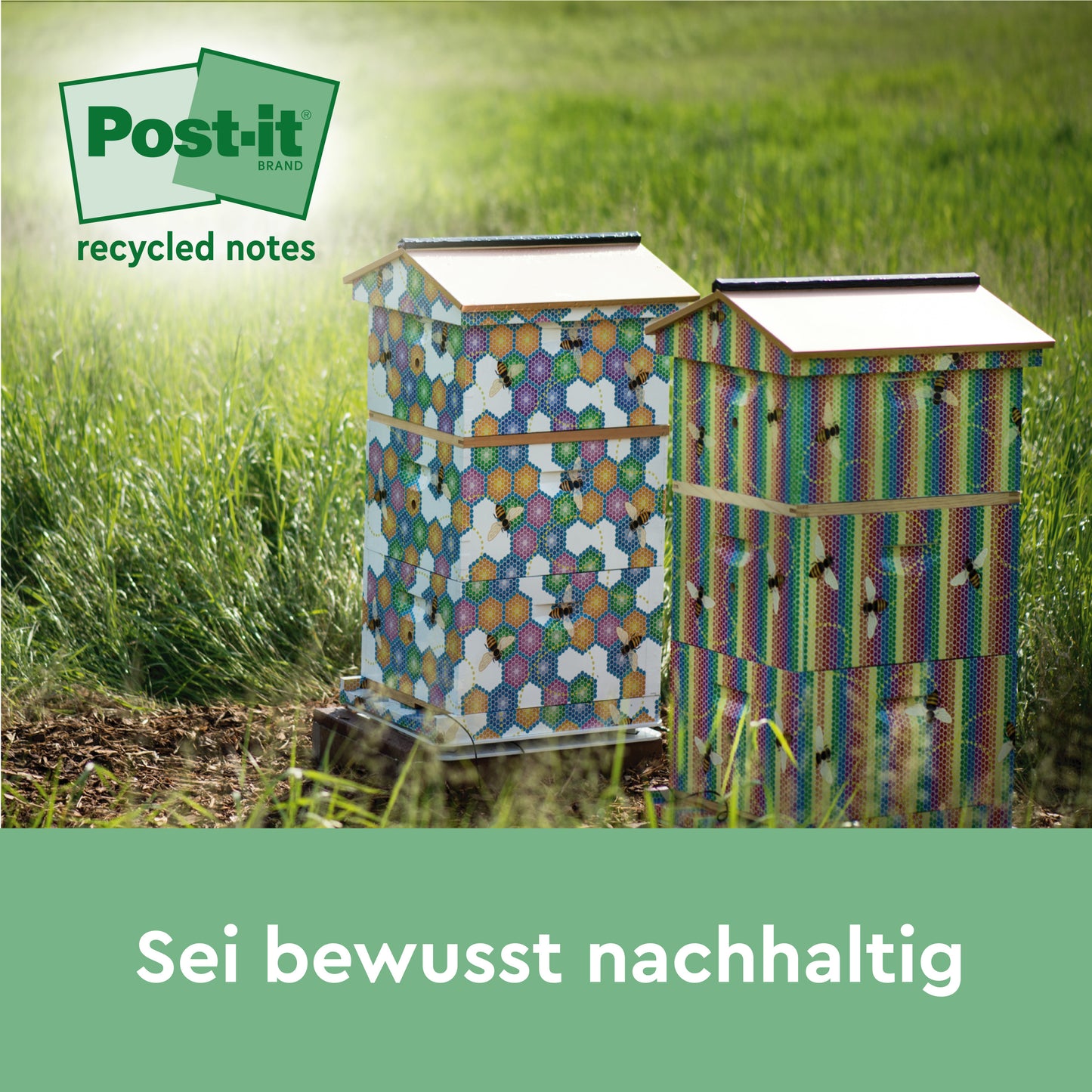 Zwei bunte Bienenstöcke mit sechseckigen Mustern stehen auf einer Wiese im Sonnenlicht. In der Ecke erscheint das Logo von Post-it® Super Sticky 100 % Recycling Notes by 3M Deutschland GmbH. Der Text darunter lautet: "Sei bewusst nachhaltig.
