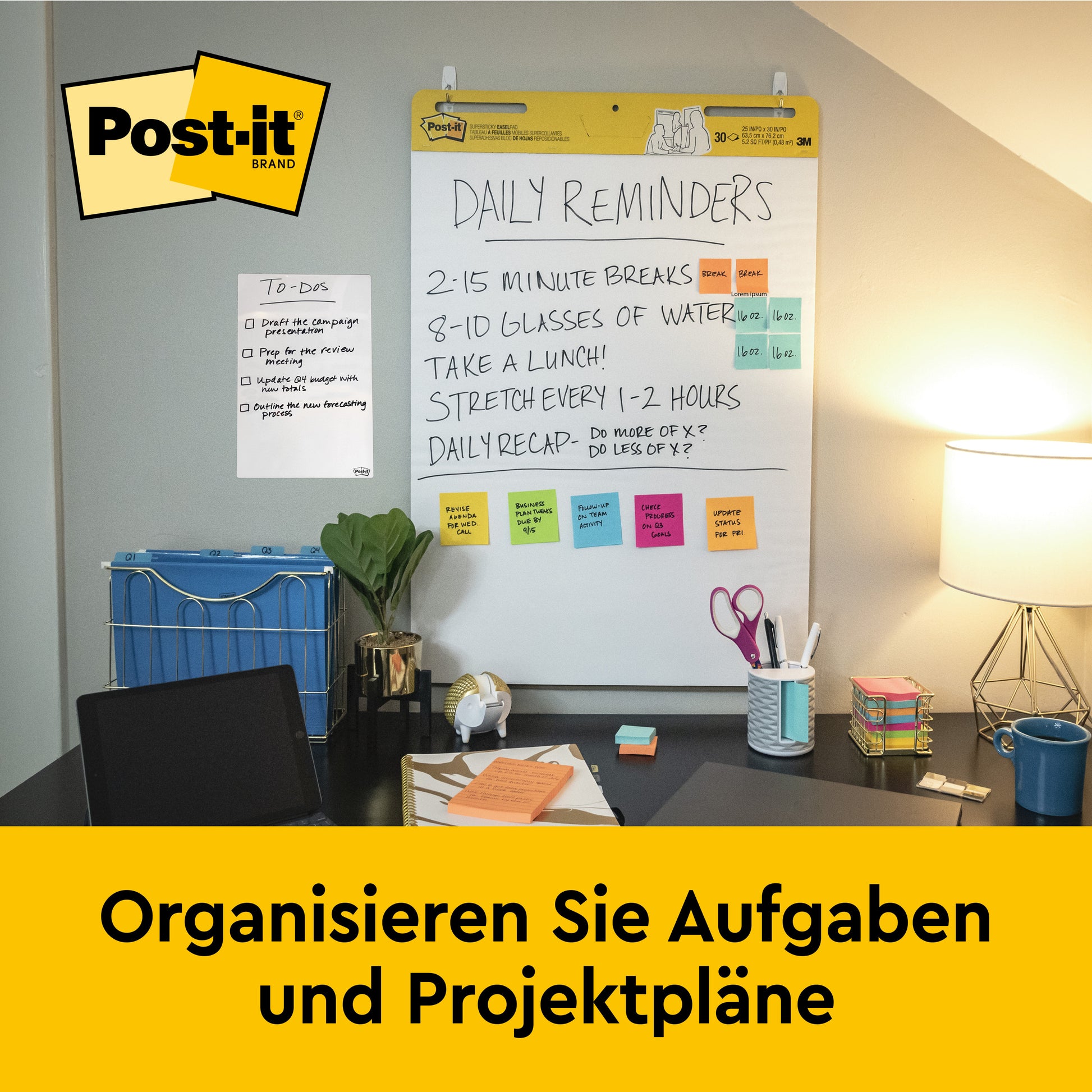 Ein Schreibtisch mit Büromaterial, Lampe und Stuhl steht vor einer an der Wand befestigten 3M Post-it® Super Sticky selbsthaftendes Meeting Chart (63,5x76,2 cm, 30 Blatt), das tägliche Erinnerungen und Notizen zeigt. Auf einem gelben Banner darunter steht "Organisieren Sie Aufgaben und Projektpläne.