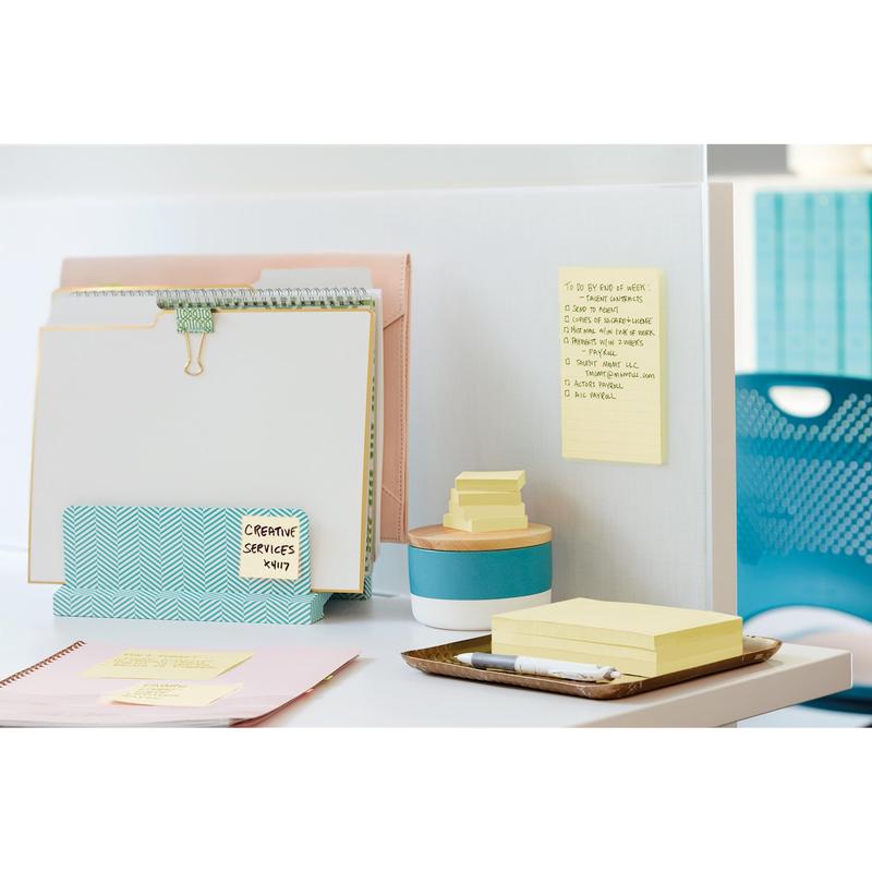 Sur un bureau blanc se trouvent des 3M Post-it® Super Sticky Notes (76 mm x 127 mm, 90 feuilles/bloc, 100% PEFC) de 3M Allemagne GmbH, fixées sur une cloison et empilées à côté d'un récipient bleu, à côté de classeurs et de fournitures de bureau.