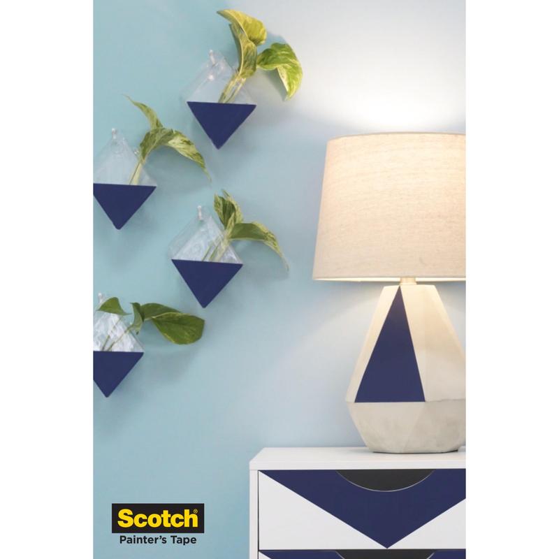 Une commode géométrique bleu-blanc et une lampe se tiennent devant un mur bleu avec des jardinières triangulaires, le tout protégé avec du Scotch® ruban de masquage pour surfaces délicates (36 mm x 41 m, 1 rouleau) de 3M Deutschland GmbH. Le logo apparaît en bas à gauche.