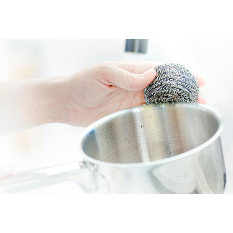 Une main utilise une spirale en acier inoxydable Scotch-Brite® de 3M Deutschland GmbH, 3 pièces par paquet, pour enlever les salissures tenaces lors du nettoyage d'une casserole en acier inoxydable.