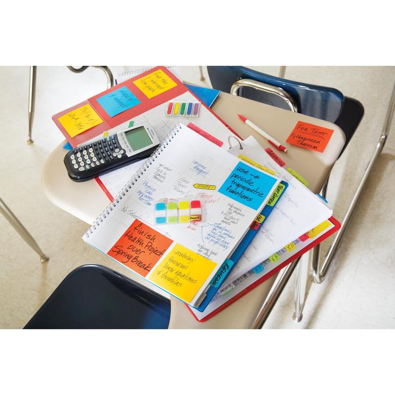 Sur un bureau de classe se trouvent des cahiers, un planificateur avec des onglets de classement 3M Post-it® Index Strong (Mini, jaune, rouge, bleu & vert), une calculatrice, des stylos, des surligneurs & des dossiers ; des chaises vides l'entourent et les onglets aident à organiser les documents.