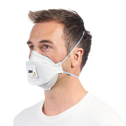 Un homme porte le masque respiratoire à particules 3M™ Aura™ Comfort Cool Flow™ 9332+ FFP3 avec valve de 3M Deutschland GmbH, fixé avec deux bandes élastiques, vu de gauche sur un fond uni blanc.