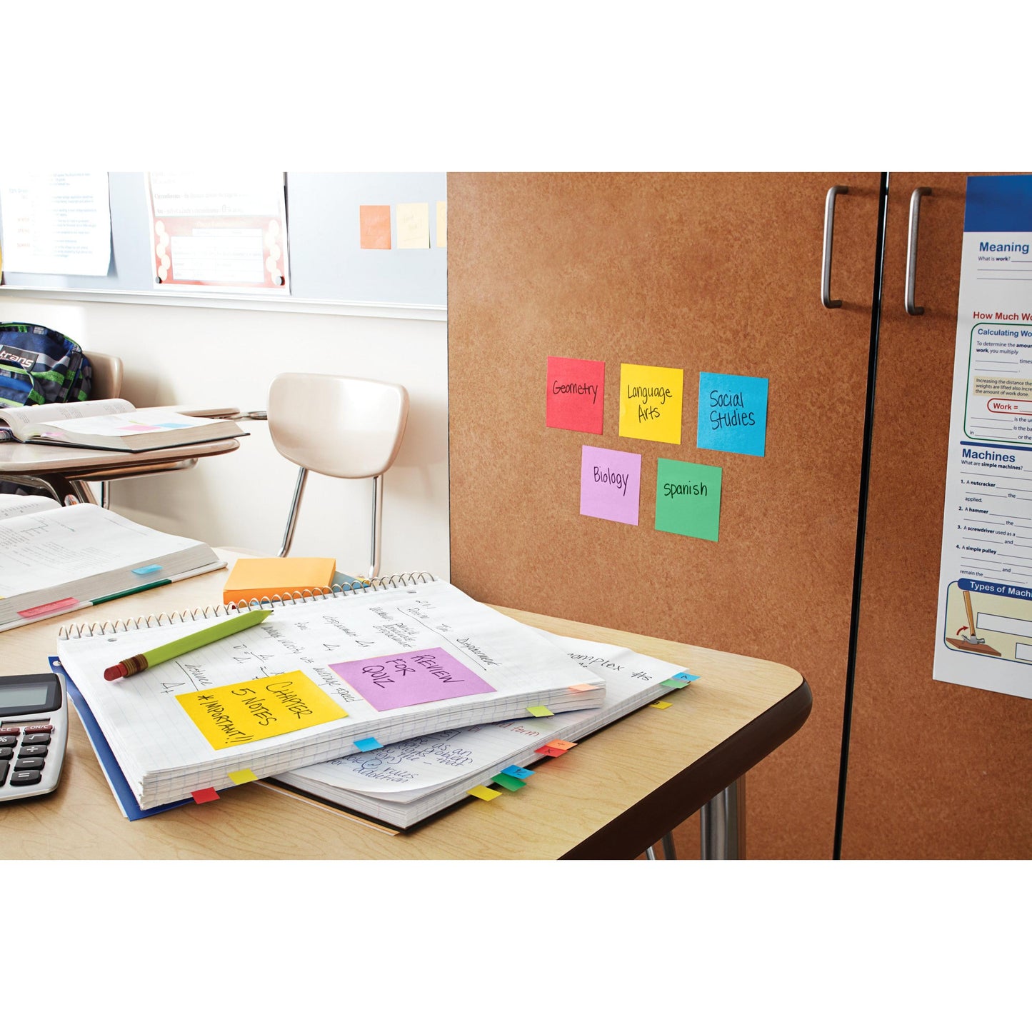 Ein Klassenzimmer mit einem hölzernen Schreibtisch, auf dem offene Hefte, ein Taschenrechner und Papiere liegen. An der Rückwand sind Post-it® Super Sticky Z-Notes (Blau, 76x76mm) von 3M Deutschland GmbH für die Fächer beschriftet; ein bärenförmiger Spender steht in der Nähe. Dahinter steht ein leerer Stuhl.
