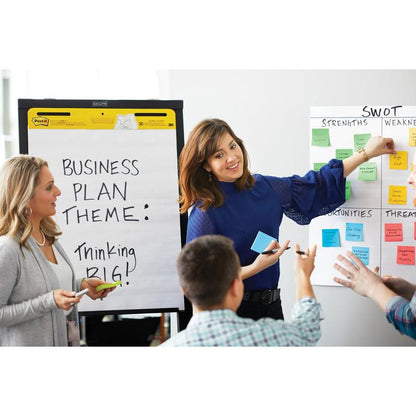 Lors d'une réunion d'affaires chez 3M Deutschland GmbH, une femme pointe sur une analyse SWOT tandis qu'une autre tient un marqueur à côté d'un tableau à feuilles avec l'inscription "Thème du plan d'affaires" : Thinking BIG!" avec des Post-it® Super Sticky Notes, 76 mm x 127 mm, 90 feuilles/bloc, 100% PEFC.