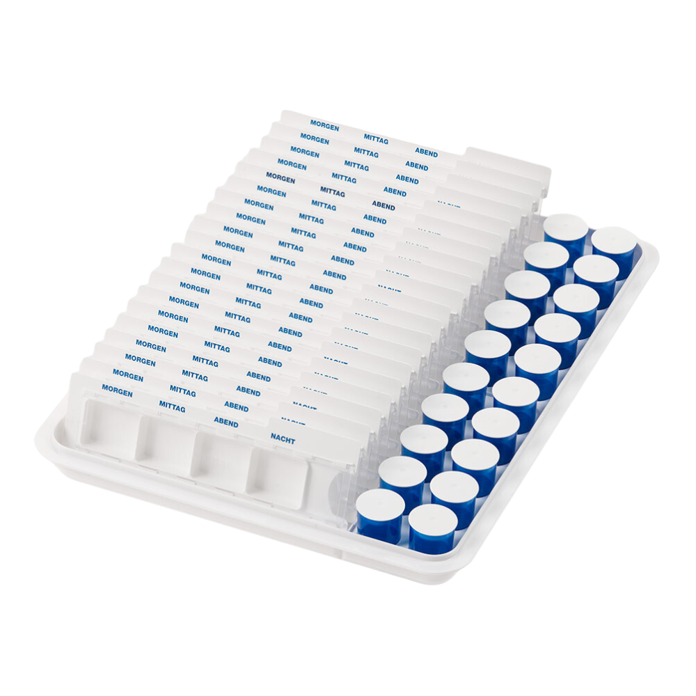 Un plateau-distributeur de gobelets mevipas de Helmut Schwarz GmbH se compose d'un plateau blanc sur lequel se trouve un organisateur de médicaments avec des rangées de compartiments pour comprimés, étiquetés en allemand : « Matin », « Midi », « Soir » et « Nuit ». À droite, il y a des conteneurs cylindriques avec des couvercles bleus, parfaits pour un stockage efficace des médicaments dans le domaine des soins.
